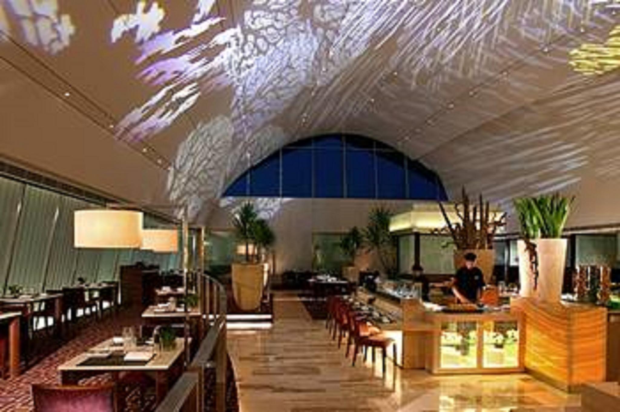 Traders Hotel, Κουάλα Λουμπούρ Εξωτερικό φωτογραφία The photo shows the interior of a modern restaurant. The space features a high ceiling with a large arched window, allowing natural light to enter. A projection of intricate designs or patterns can be seen on the ceiling, adding a decorative touch. T