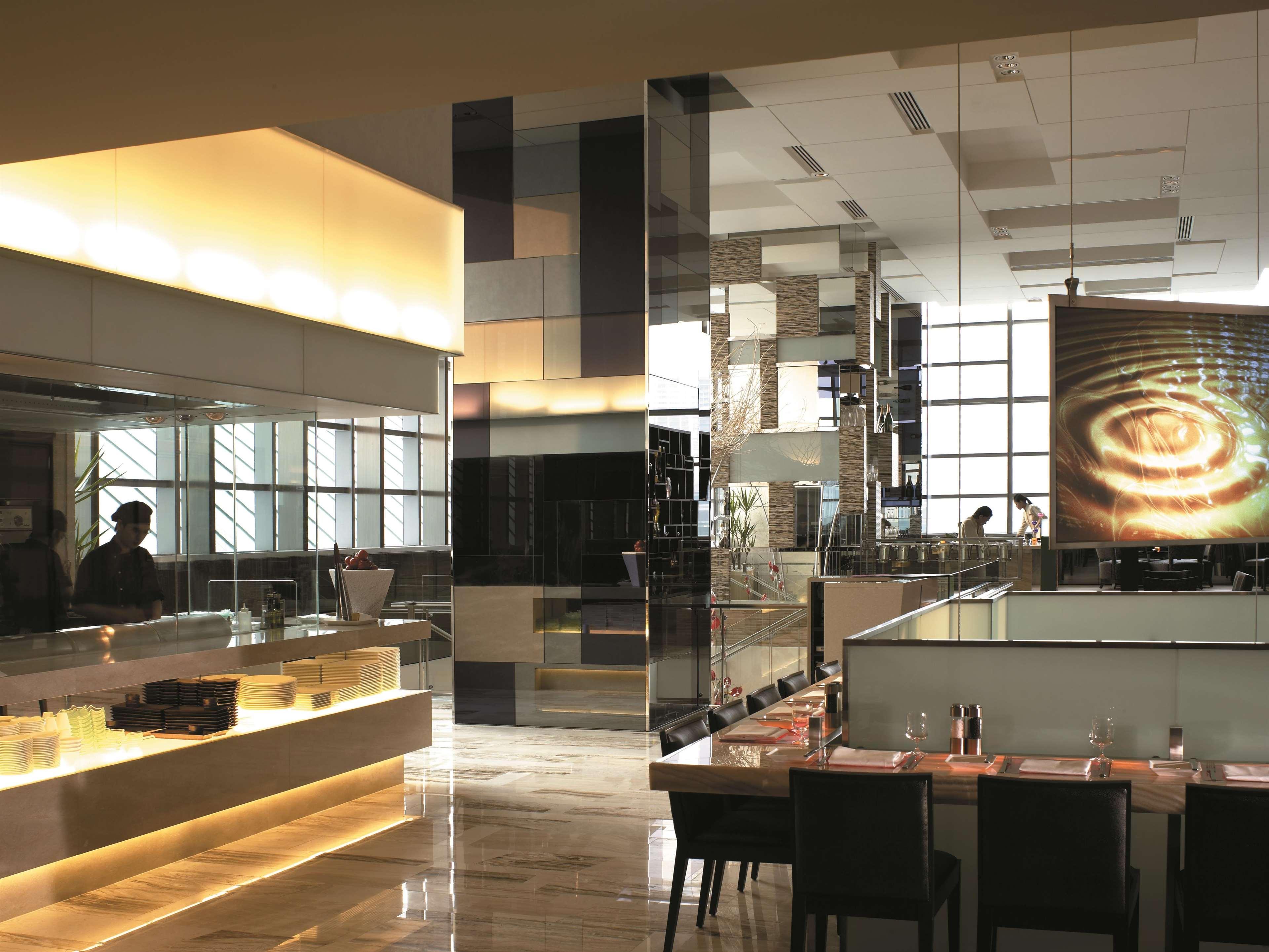 Traders Hotel, Κουάλα Λουμπούρ Εξωτερικό φωτογραφία The photo shows a modern restaurant interior. It features a sleek design with glossy surfaces and warm lighting. The space includes a counter area with a well-lit service section, and a dining area with dark wooden tables and chairs. Large windows al