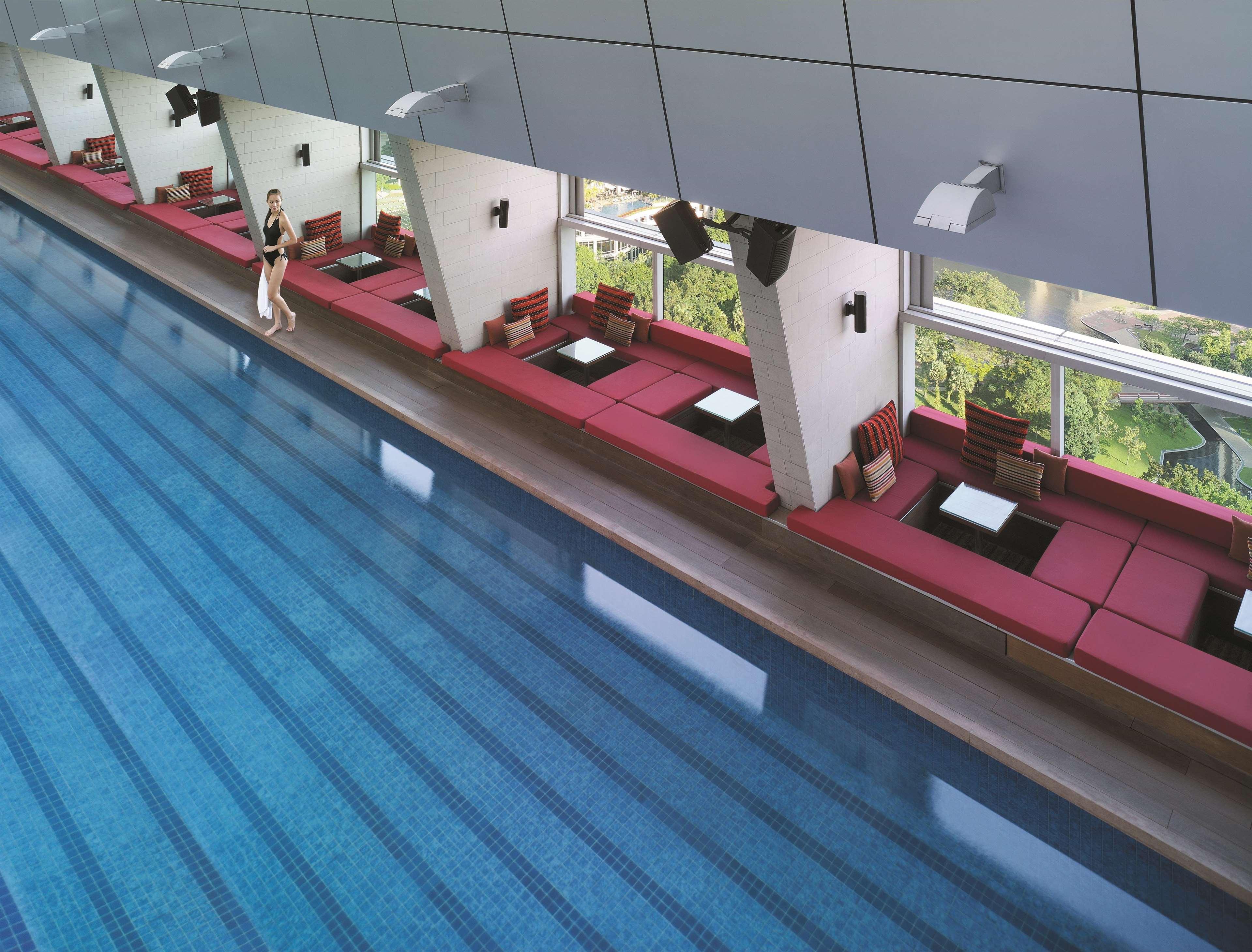 Traders Hotel, Κουάλα Λουμπούρ Εξωτερικό φωτογραφία The photo shows an indoor swimming pool with a modern design. On one side of the pool, there are seating areas with red cushions and small tables. The surroundings have large windows that allow natural light to enter, providing a view of greenery out