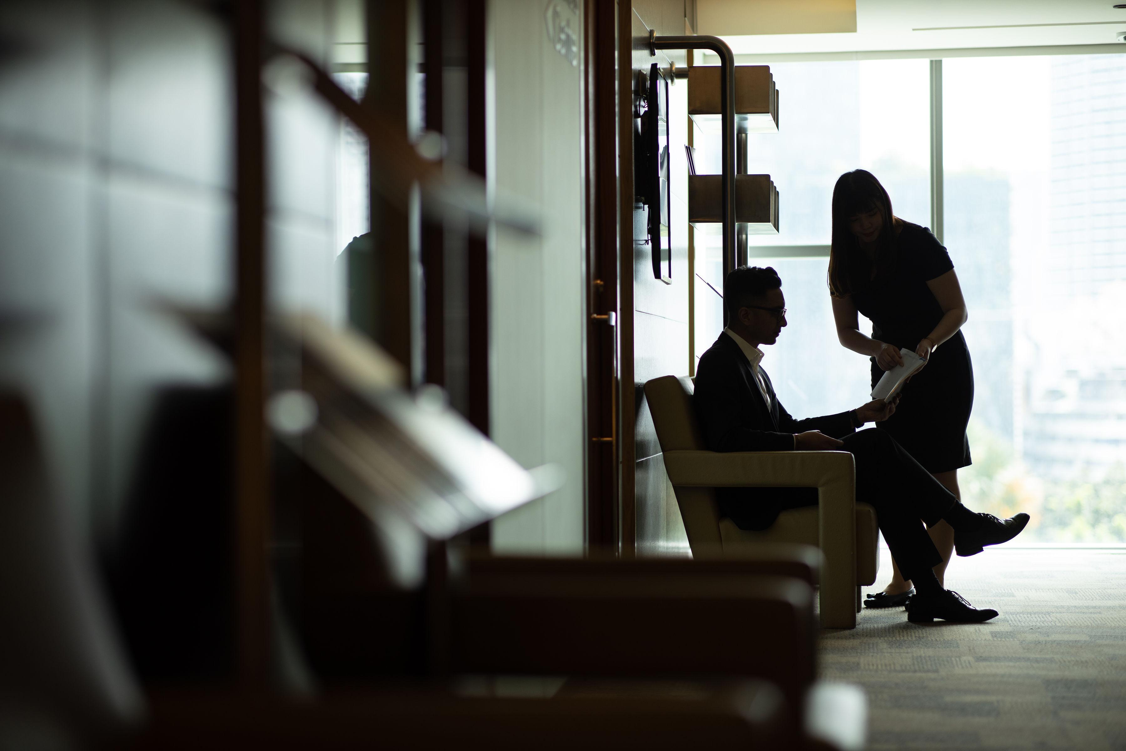Traders Hotel, Κουάλα Λουμπούρ Εξωτερικό φωτογραφία The photo shows two people in an office setting. One person, seated in a chair, is dressed in formal attire, while the other person, standing nearby, appears to be discussing something with them, possibly looking at documents. The scene is backlit, c
