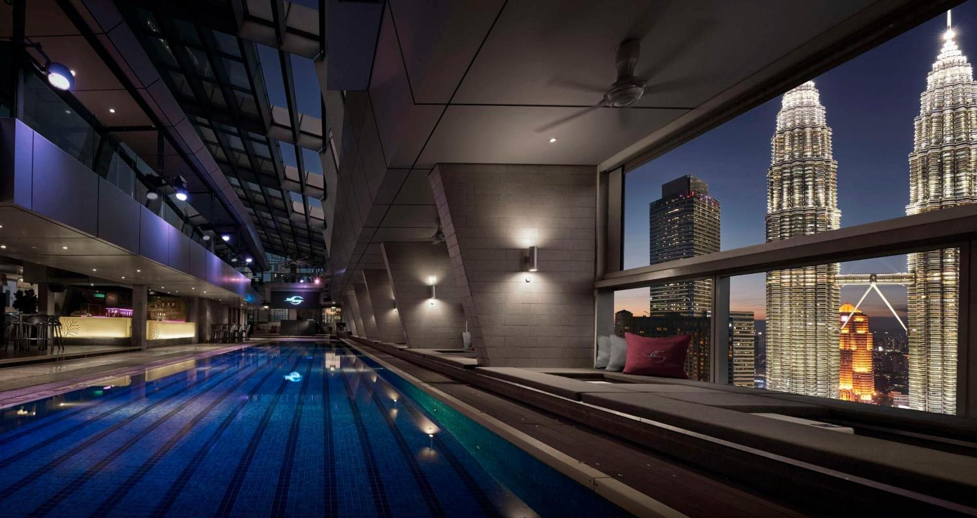 Traders Hotel, Κουάλα Λουμπούρ Εξωτερικό φωτογραφία The image showcases a luxurious indoor swimming pool with an elegant design. The pool is illuminated by soft lighting, and large windows provide a stunning view of a city skyline featuring tall skyscrapers, including a prominent building with a uniqu