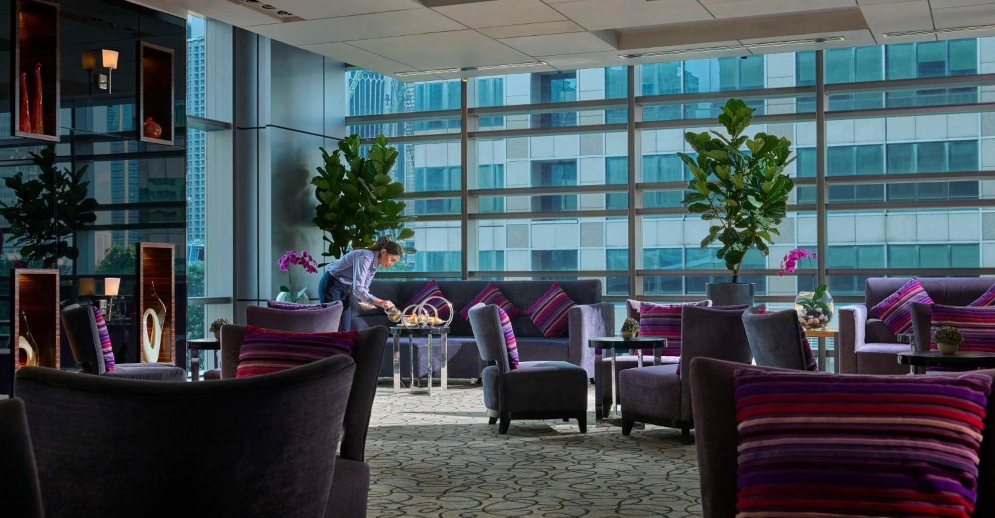 Traders Hotel, Κουάλα Λουμπούρ Εξωτερικό φωτογραφία The photo shows a stylish and modern interior of a lounge or waiting area. It features plush seating arrangements with dark chairs and sofas, adorned with colorful striped cushions. Large plants and orchids add a touch of greenery to the space. There