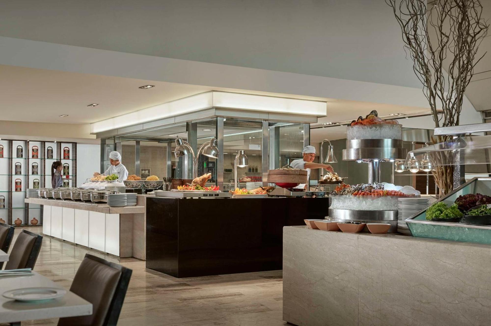 Traders Hotel, Κουάλα Λουμπούρ Εξωτερικό φωτογραφία The photo shows a modern buffet-style restaurant or dining area. There is a large, well-organized food display featuring a variety of dishes, prominently positioned on a central serving counter. The food appears to be attractively arranged, with opti